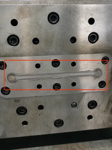 Stamped stainless steel connecting plate inside the blanking die, showing burr formation along the shear edge
